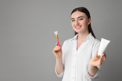 Cosmetologist with cosmetic product and silicone brush on grey background, space for text