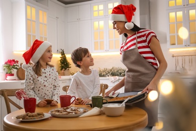 Mother giving her cute little children freshly baked Christmas cookies in kitchen