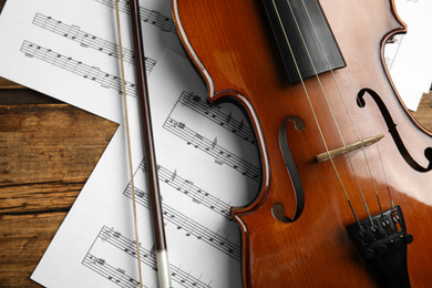 Photo of Beautiful violin, bow and note sheets on wooden table, flat lay