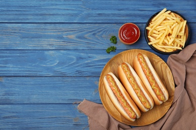 Composition with hot dogs, fries and sauce on color wooden table, top view. Space for text