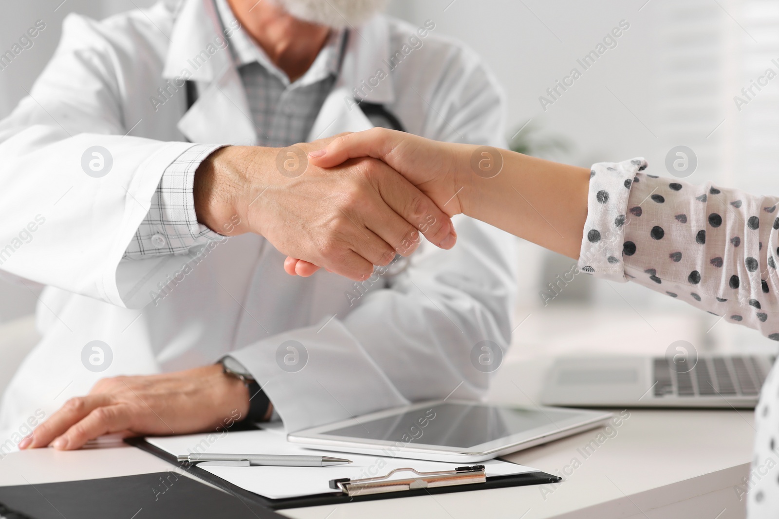 Photo of Senior doctor shaking hands with patient in clinic, closeup