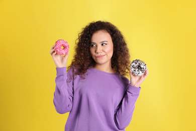 Photo of Beautiful African-American woman with donuts on yellow background