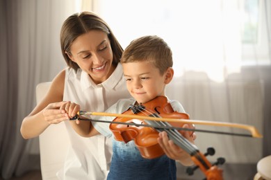 Photo of Young woman teaching little boy to play violin indoors