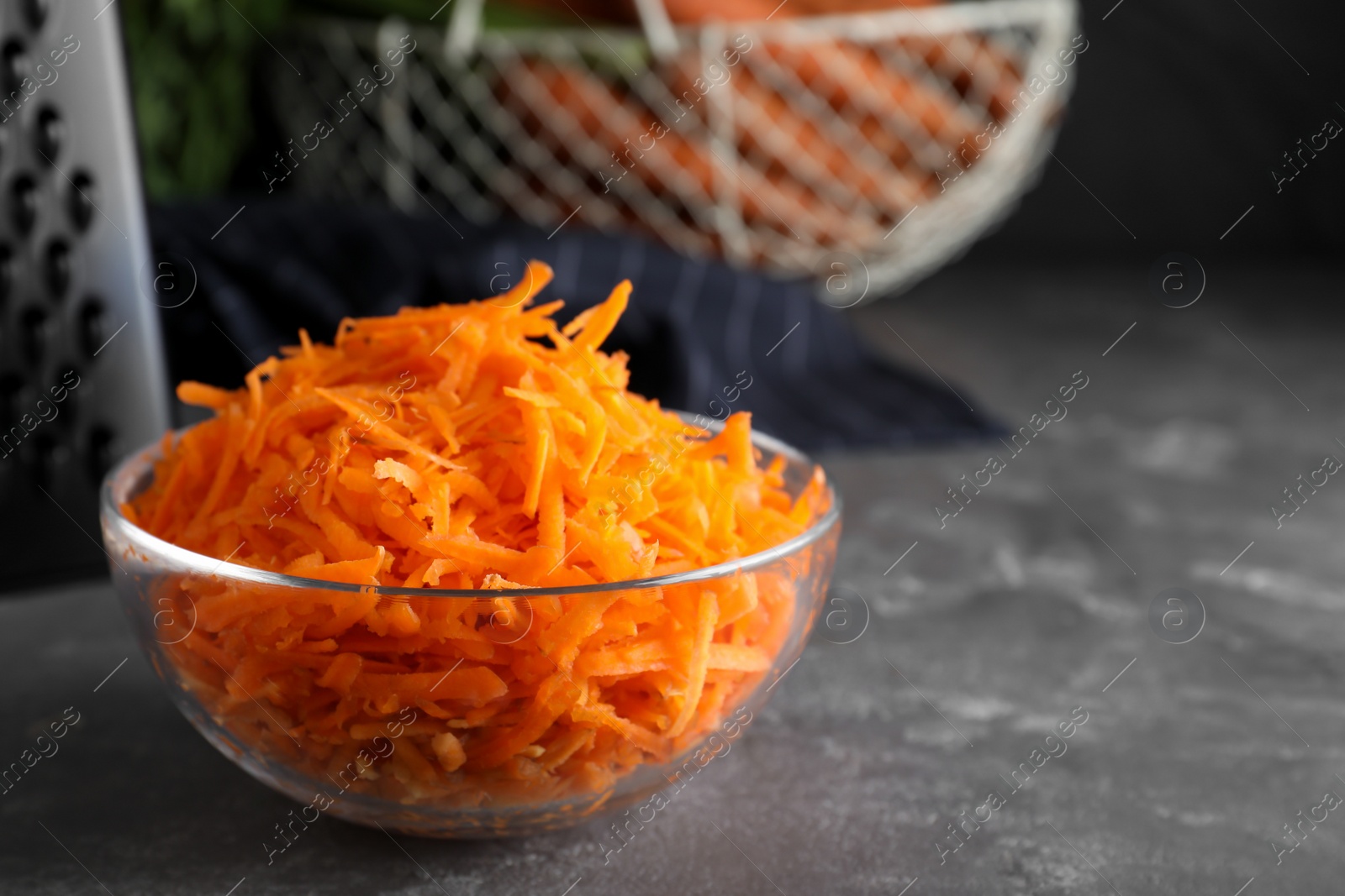 Photo of Glass bowl with grated carrot on grey table, closeup