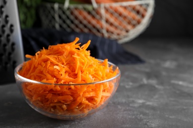 Glass bowl with grated carrot on grey table, closeup