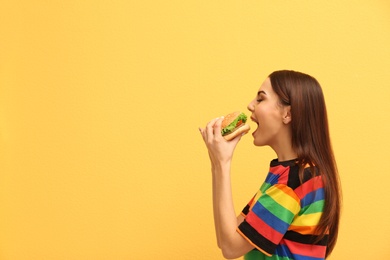 Young woman eating tasty burger on color background. Space for text