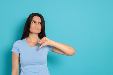 Young woman showing thumb down on light blue background, space for text