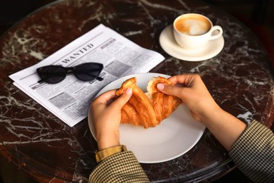 Photo of Woman breaking tasty croissant at black table, closeup