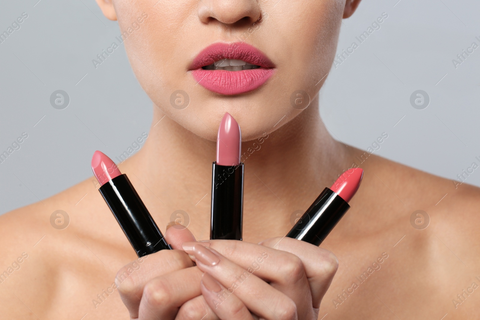 Photo of Young woman with lipsticks on gray background, closeup