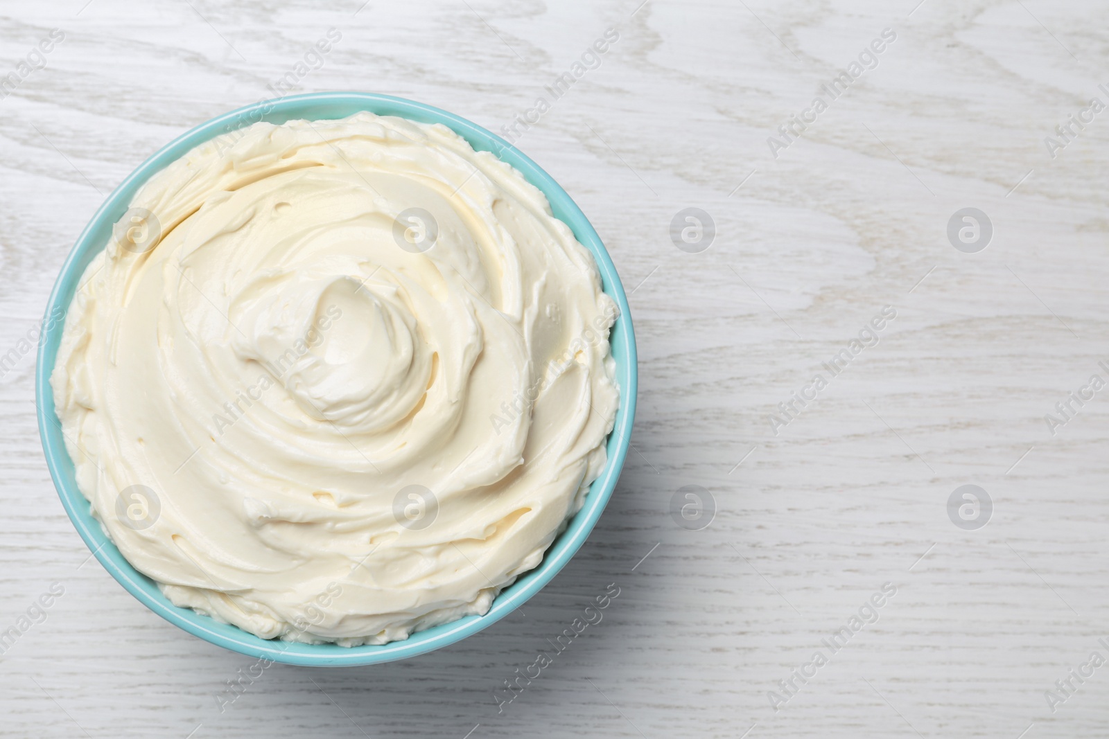 Photo of Bowl of tasty cream cheese on white wooden table, top view. Space for text