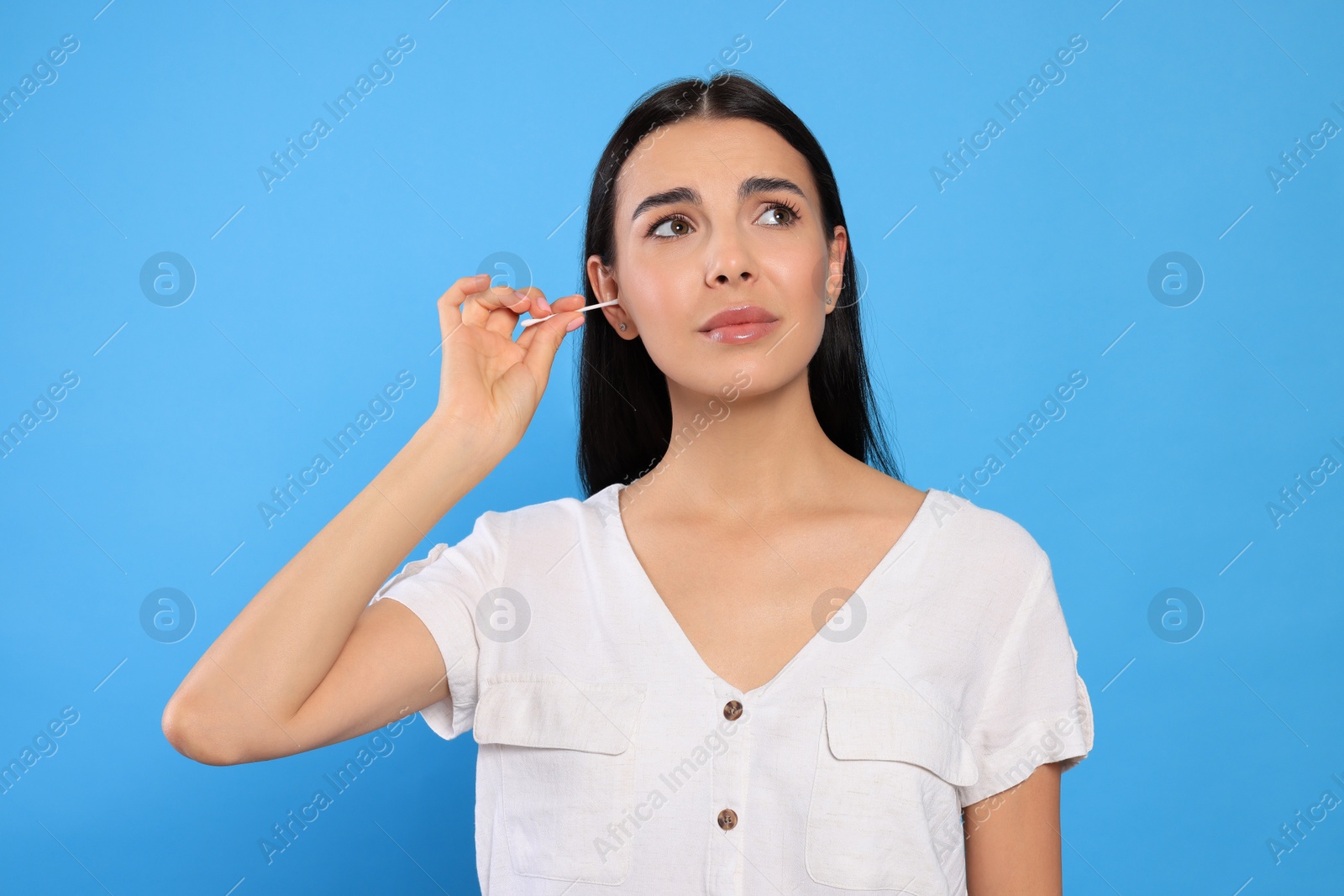 Photo of Young woman cleaning ear with cotton swab on light blue background