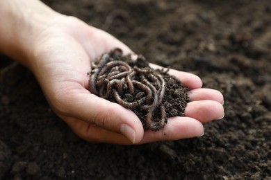 Photo of Woman holding soil with earthworms above ground, closeup