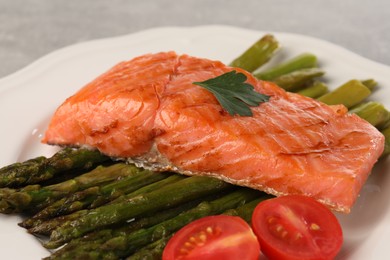 Photo of Tasty grilled salmon with tomatoes and asparagus on plate, closeup