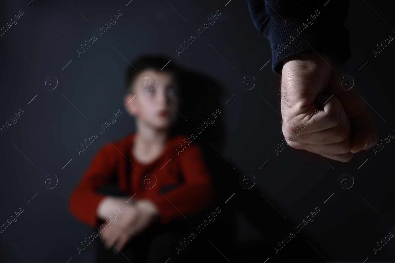 Photo of Man threatens his son on black background, focus on fist. Domestic violence concept