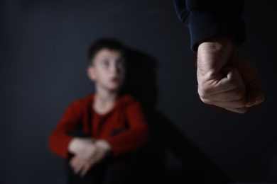 Photo of Man threatens his son on black background, focus on fist. Domestic violence concept