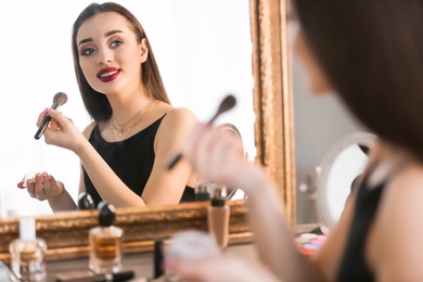 Portrait of beautiful woman applying makeup near mirror indoors