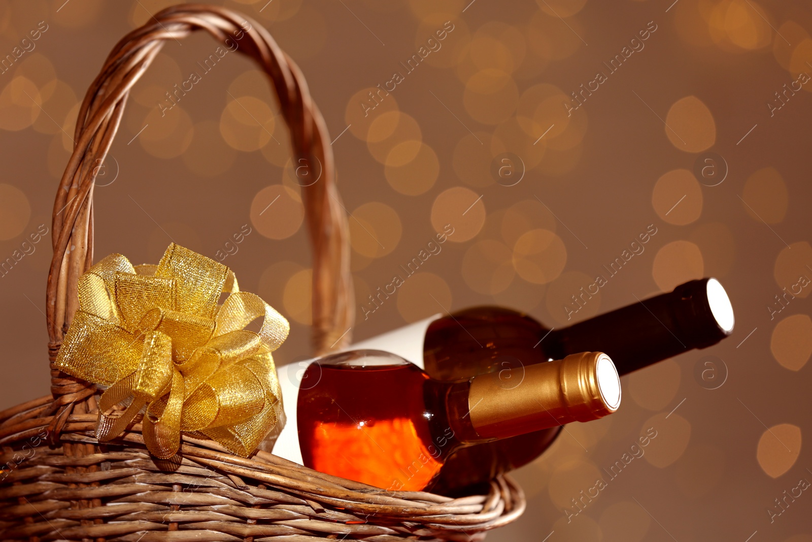 Photo of Bottles of wine in wicker basket with bow against blurred lights