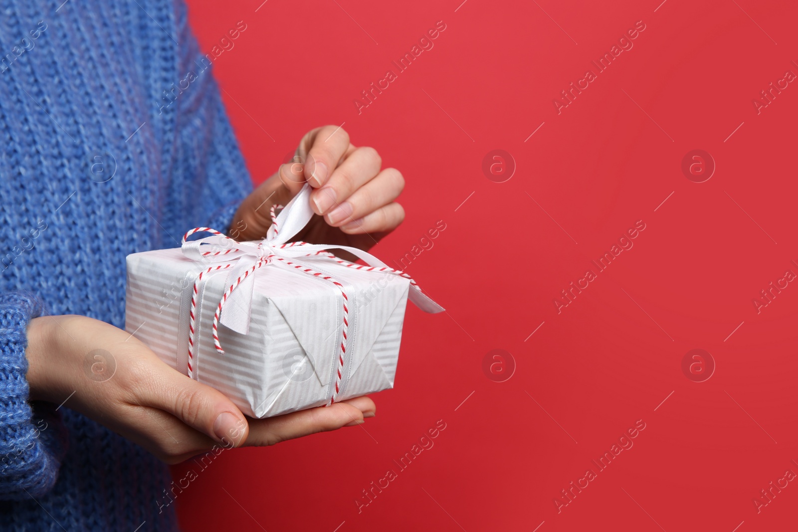 Photo of Woman holding Christmas gift box on red background, closeup. Space for text