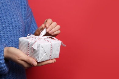 Photo of Woman holding Christmas gift box on red background, closeup. Space for text