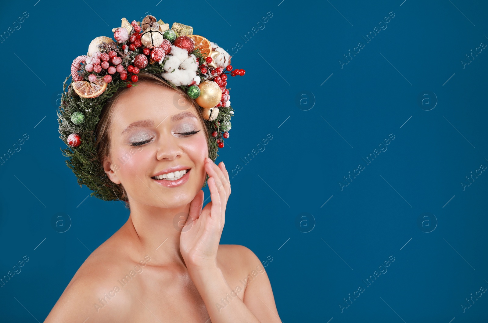 Photo of Beautiful young woman wearing Christmas wreath on blue background. Space for text