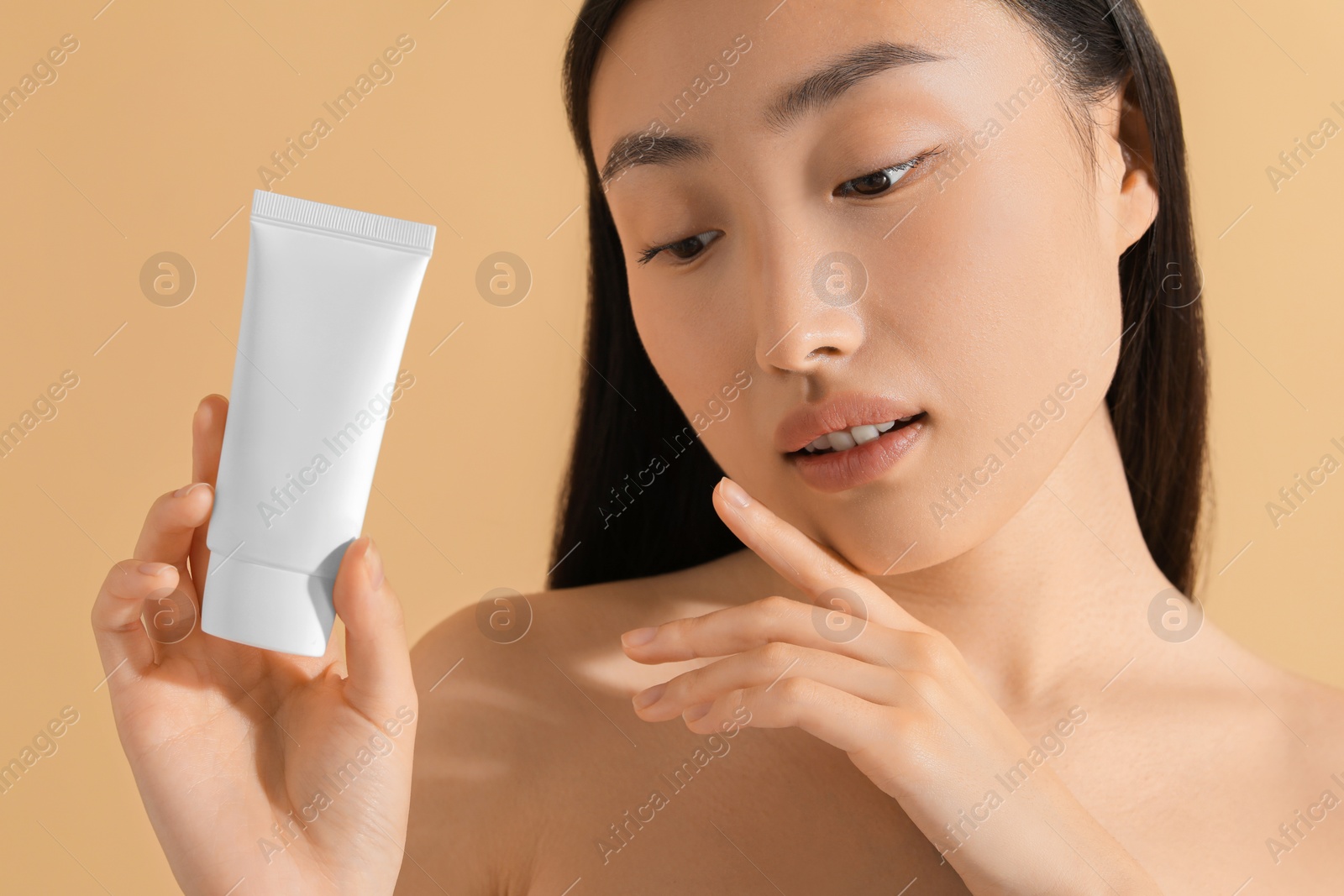 Photo of Beautiful young woman holding sun protection cream on beige background, closeup