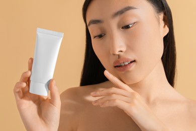 Beautiful young woman holding sun protection cream on beige background, closeup