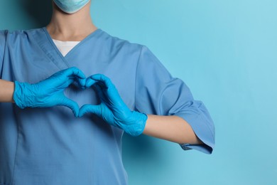 Photo of Doctor making heart with hands on light blue background, closeup. Space for text