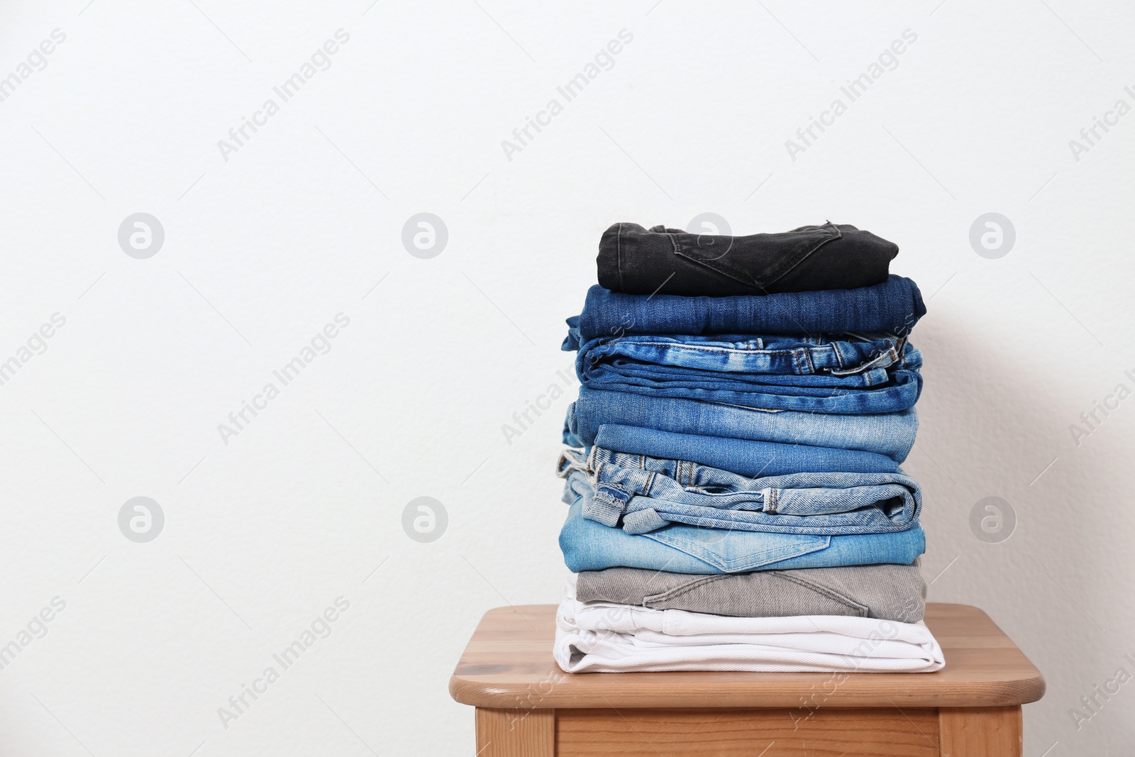 Photo of Stack of different jeans on table against white background. Space for text