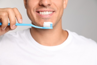 Photo of Man holding toothbrush with paste on light background, closeup