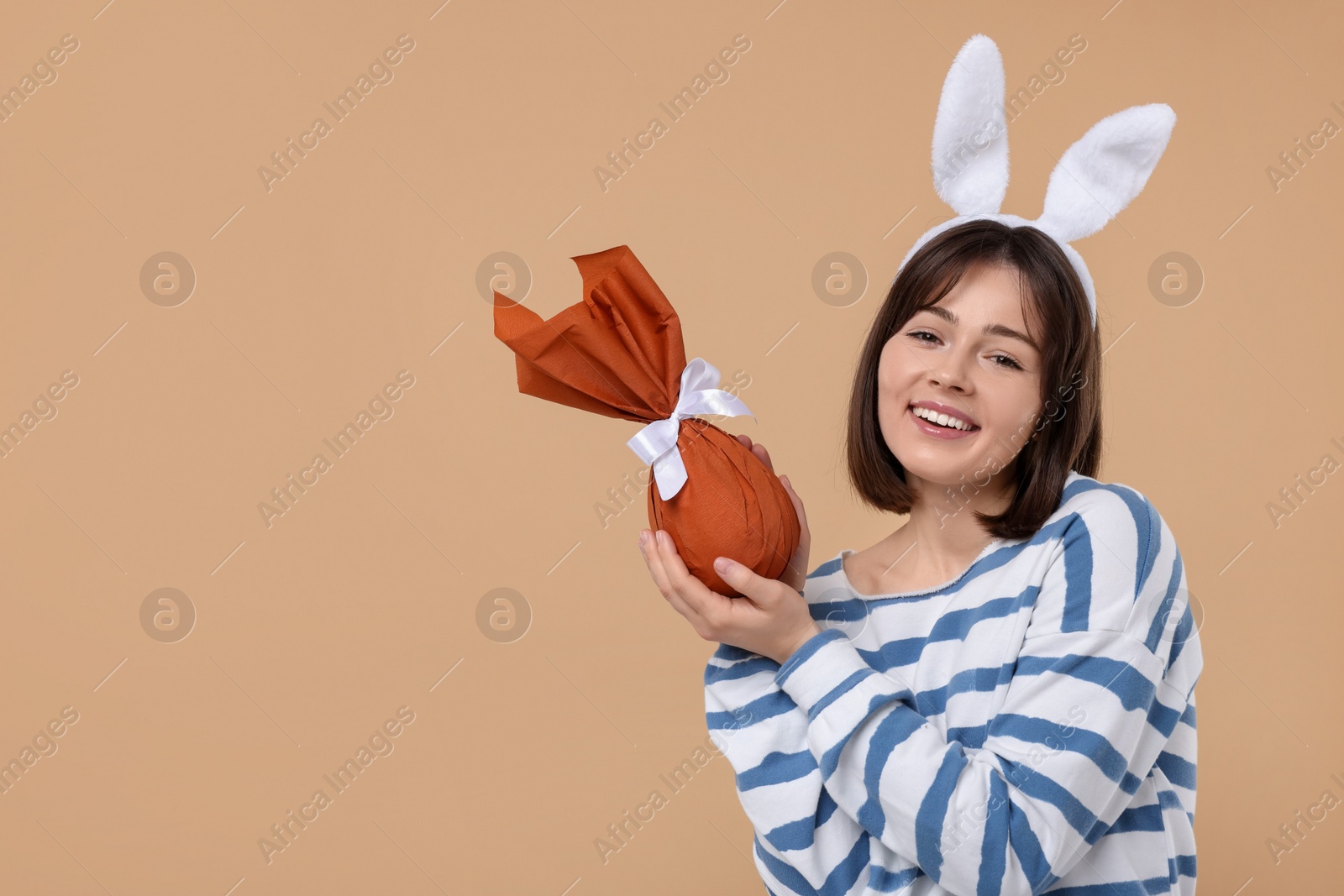 Photo of Easter celebration. Happy woman with bunny ears and wrapped egg on beige background, space for text