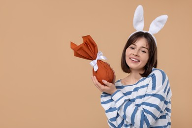 Easter celebration. Happy woman with bunny ears and wrapped egg on beige background, space for text