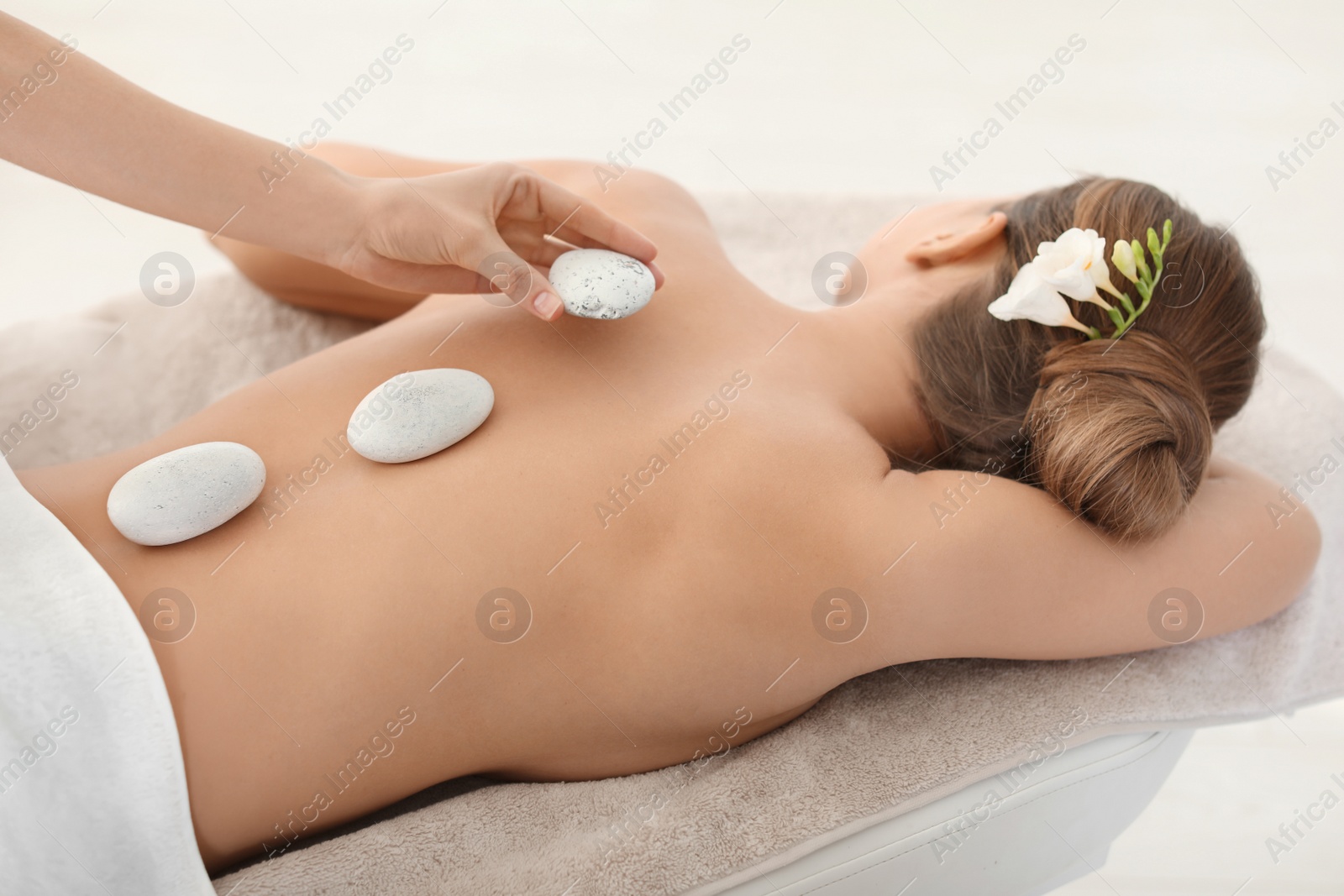 Photo of Young woman having traditional hot stones massage in spa salon