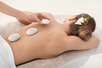 Photo of Young woman having traditional hot stones massage in spa salon