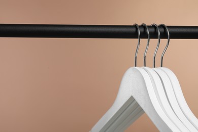 Photo of Empty clothes hangers on rack against light brown background, closeup. Space for text