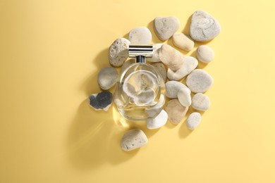 Bottle of luxury perfume in sunlight and stones on golden background, flat lay. Space for text