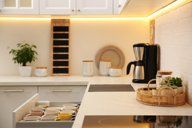 Open drawer with cups and coffeemaker on countertop in kitchen