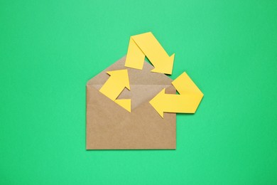 Photo of Open envelope and recycling symbol on green background, top view