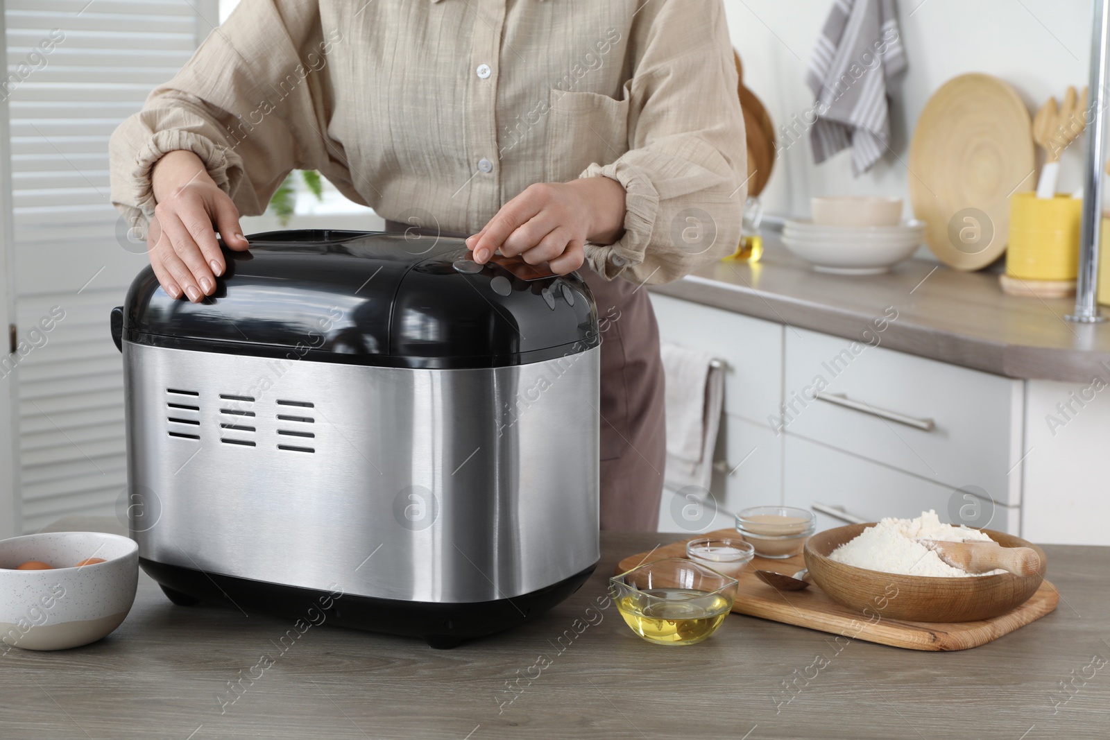 Photo of Woman using breadmaker at wooden table in kitchen, closeup