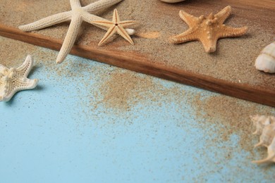 Wooden plank with beautiful starfishes, sea shells and sand on light blue background. Space for text