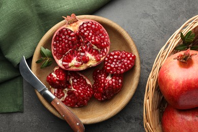 Photo of Fresh pomegranates, green leaves and knife on grey table, top view