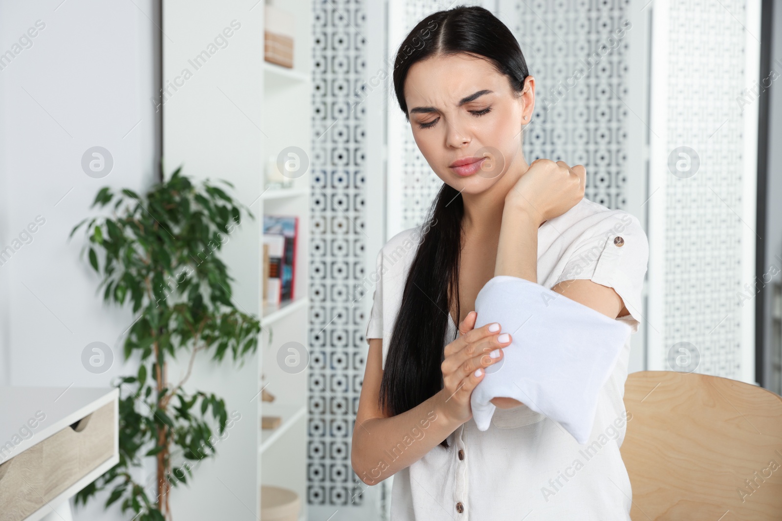 Photo of Young woman using heating pad at home