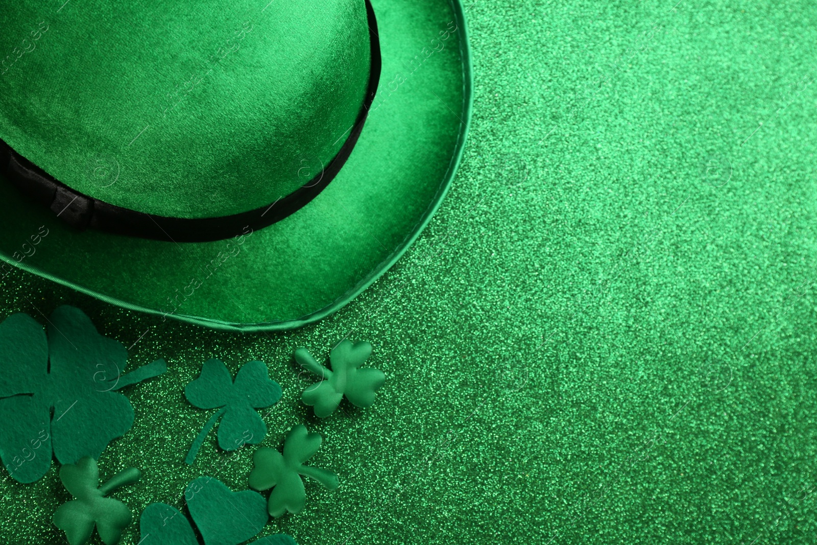 Photo of Leprechaun hat and decorative clover leaves on green glitter background, flat lay with space for text. St Patrick's Day celebration