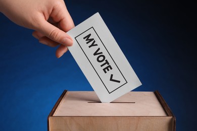 Woman putting paper with text My Vote and tick into ballot box on dark blue background