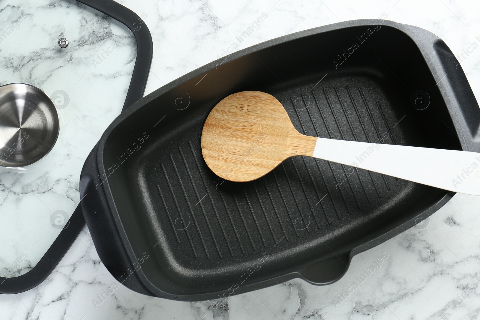 Photo of Black pot with glass lid and round spatula on white marble table, flat lay