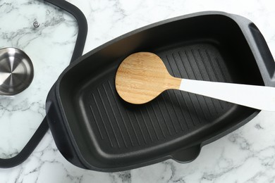 Photo of Black pot with glass lid and round spatula on white marble table, flat lay