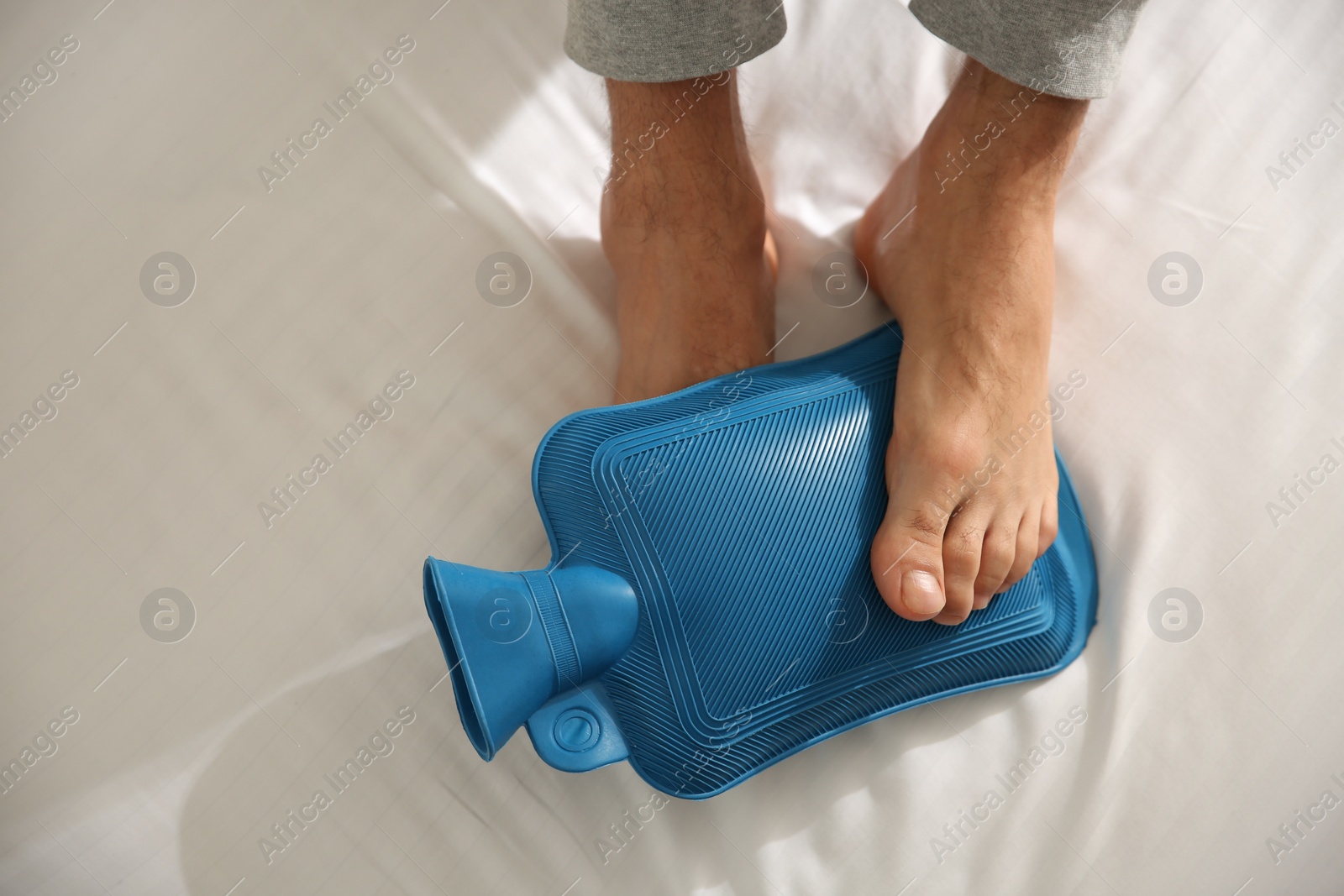 Photo of Man warming feet with hot water bottle on bed, closeup