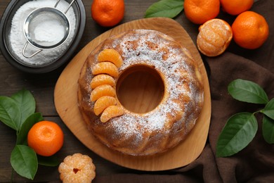 Homemade yogurt cake with tangerines, powdered sugar and green leaves on wooden table, flat lay