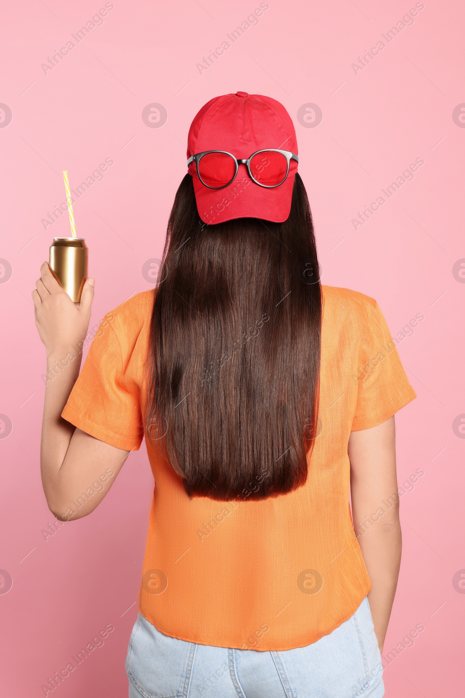 Photo of Woman holding tin can with beverage on pink background, back view