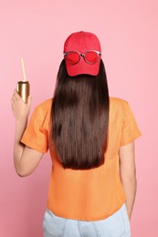 Woman holding tin can with beverage on pink background, back view