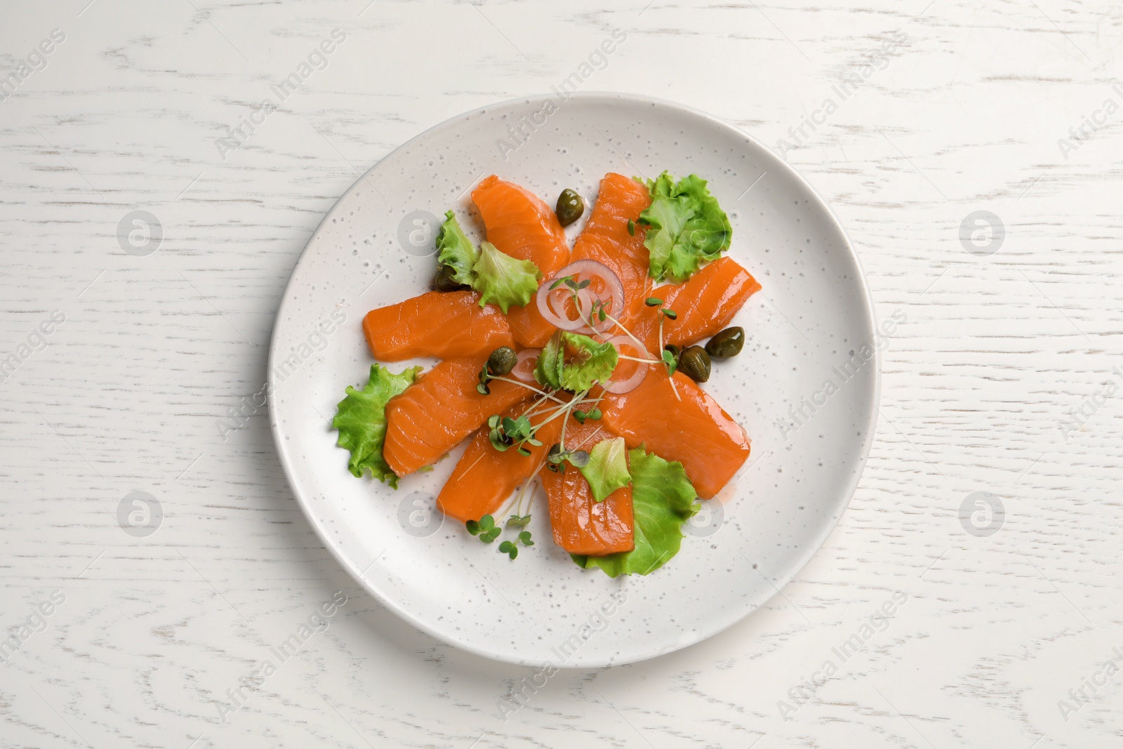 Photo of Salmon carpaccio with capers, lettuce, microgreens and onion on white wooden table, top view